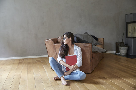 Young woman sitting with book on wooden floor at home