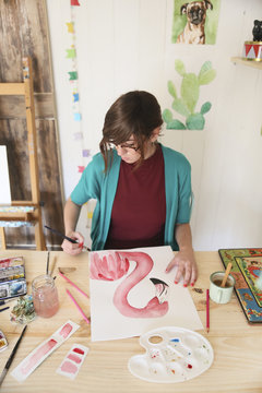 Woman painting aquarelle of a flamingo on desk in her studio