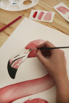 Woman's hand painting aquarelle of a flamingo on desk in her studio