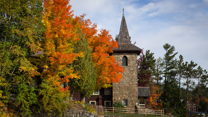 A stone church steeple surrounded by colorful autumn foliage on a sunny fall day in the village of Lake Placid, New York