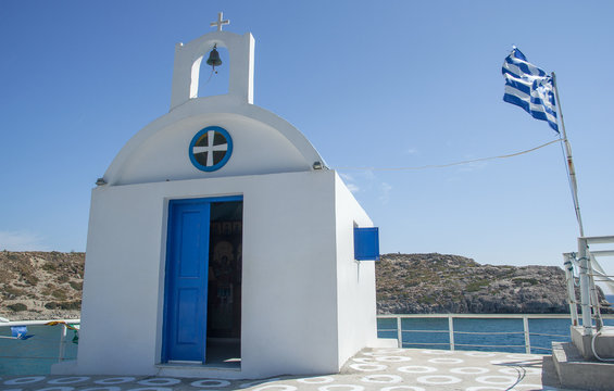 Chapel and greek flag in Kolymbia harbor, Rhodes, Greece