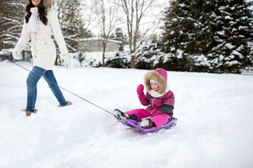 happy mother pulling sled with child in winter