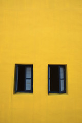 Fototapeta na wymiar Two wooden windows on the yellow facade