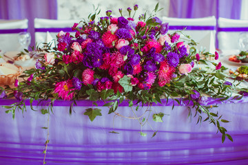 Huge garland made of violet and pink flowers stands on the dinne