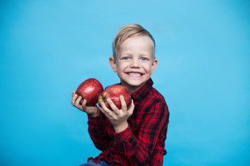 Handsome little kid with fruits. Studio portrait over blue background