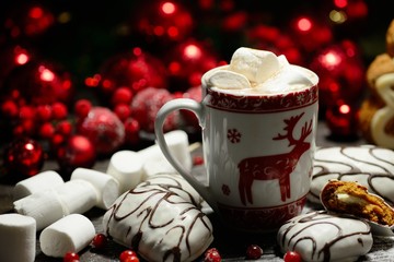 Hot chocolate or cocoa beverage with cinnamon and gingerbread cookies in snowon vintage wooden table background.