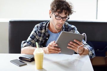 man with tablet pc and earphones sitting at cafe