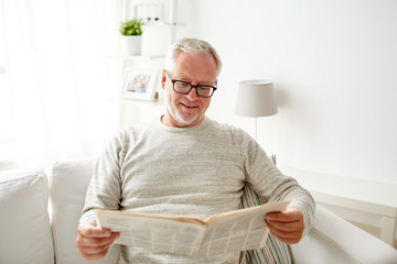 senior man in glasses reading newspaper at home