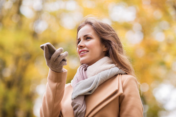 woman recording voice on smartphone in autumn park