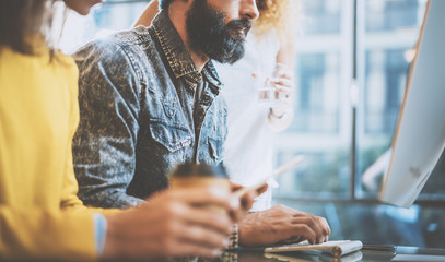 Bearded man typing on desktop keyboard in a office. Young coworkers discussing business ideas at workplace.Horizontal,blurred.