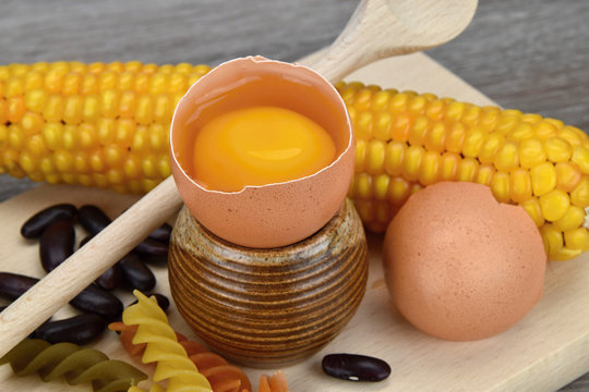 Open egg around corn, pasta and beans on a cutting board. Yolk and albumen.