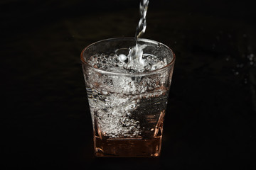 Water in glass with water splash on black background