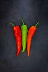 Two red and one green peppers on a gray slate