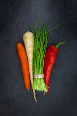 Carrots parsley chives and red pepper on a gray slate
