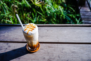 Close up of ice coffee with whip cream and caramel on top on wood bar in cafe