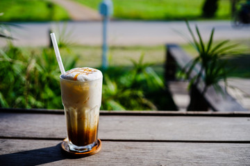 Close up of ice coffee with whip cream and caramel on top on wood bar in cafe