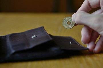 Male hand holding a bronze coin of five Yens (Japanese Yen, JPY) and withdrawing that from the brown leather wallet 