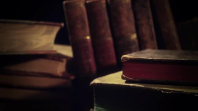 Old, aged books in a row on a wooden table. Camera panning and moving. Closeup.