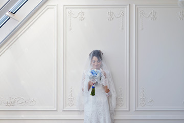 Beauty bride in bridal gown with bouquet and lace veil indoors. Beautiful model girl in a white wedding dress. Female portrait of cute lady. Woman with hairstyle