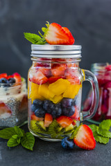 Fruit salad and fresh berries fruit in a glass jars on stone background. Organic food and detox.