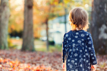 Toddler girl standing outside in the fall leaves at sunset