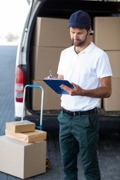 Delivery man writing on clipboard while standing next to his van