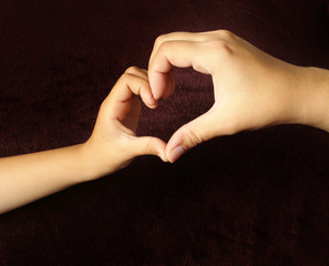 Mother and child made a heart with his hands on a dark background. Adult and children's hands make a heart.