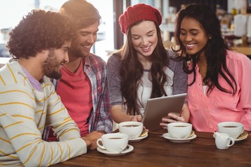 Group of friends using digital tablet while having cup of coffee
