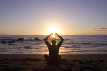 Frau formt Herz mit H&auml;nden am Strand mit Sonnenuntergang
