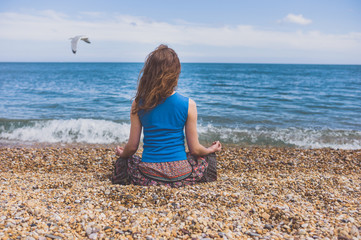 Fototapeta na wymiar Young woman meditating on the beach