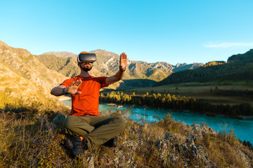 Successful young man, using virtual reality goggles to tour in mountains, on vacation in summer