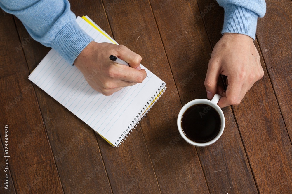 Poster man holding a cup of coffee and writing on notepad