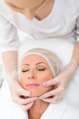 Fototapeta na wymiar Mature lady lying during facial examination at spa
