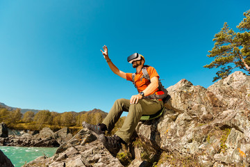 Successful young man, using virtual reality goggles to tour in mountains, on vacation in summer