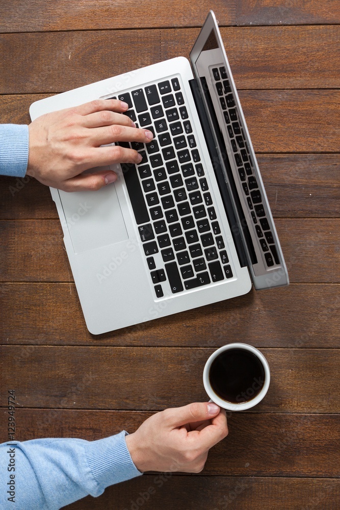 Poster man using laptop while having cup of coffee
