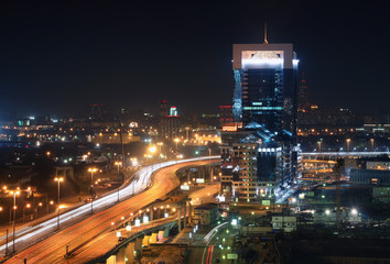 Obraz premium Modern office building next to the road overpass on the background of the industrial area by night. Focus on building