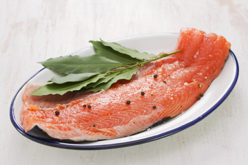 raw salmon with black pepper and bay leaf on white dish on white wooden background