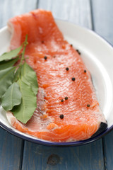 raw salmon with black pepper and bay leaf on white dish on blue wooden background