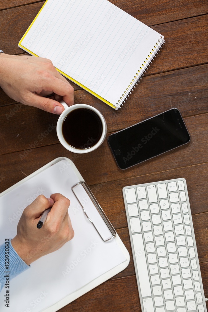 Poster man writing on clipboard while having cup of coffee