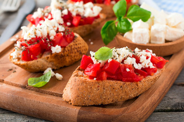 Bruschetta with tomatoes, feta cheese and basil. Traditional Greek snack on wooden background. Selective focus.