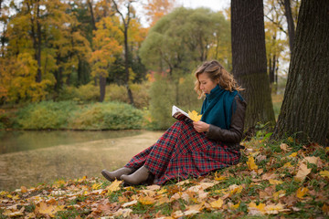 Beautiful girl in autumn forest reading a book sitting under a tree