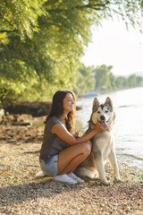 Young brunette woman playing with her dog on the riverbank.