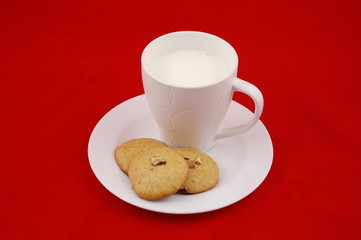 Milk and cookies. A mug of milk and a few home made ginger bread and walnuts cookies on a plate, isolated on red background.Christmas morning. 