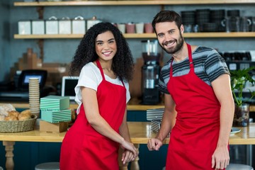 Portrait of smiling waiter and waitress leaning at counter