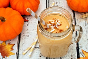 Pumpkin smoothie in a mason jar with coconut and cinnamon, scene on rustic white wood