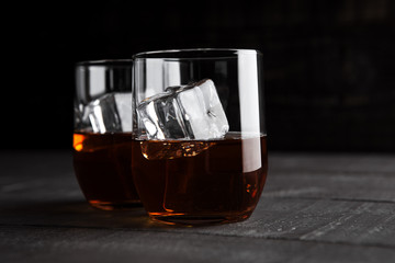 Glasses of whiskey with ice on wooden background