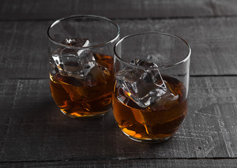 Glasses of whiskey with ice on wooden background
