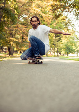 Skateboarder squatting on a skate and ride through the forest