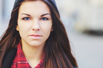 Naklejka premium A pretty young blue-eyed brunette girl with long hair in a red plaid shirt and black hat, outdoors, close-up.
