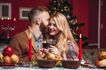 Beautiful couple in a decorated festive interior with a Christmas tree drinking wine. A romantic dinner for thanksgiving with fried chicken and candles